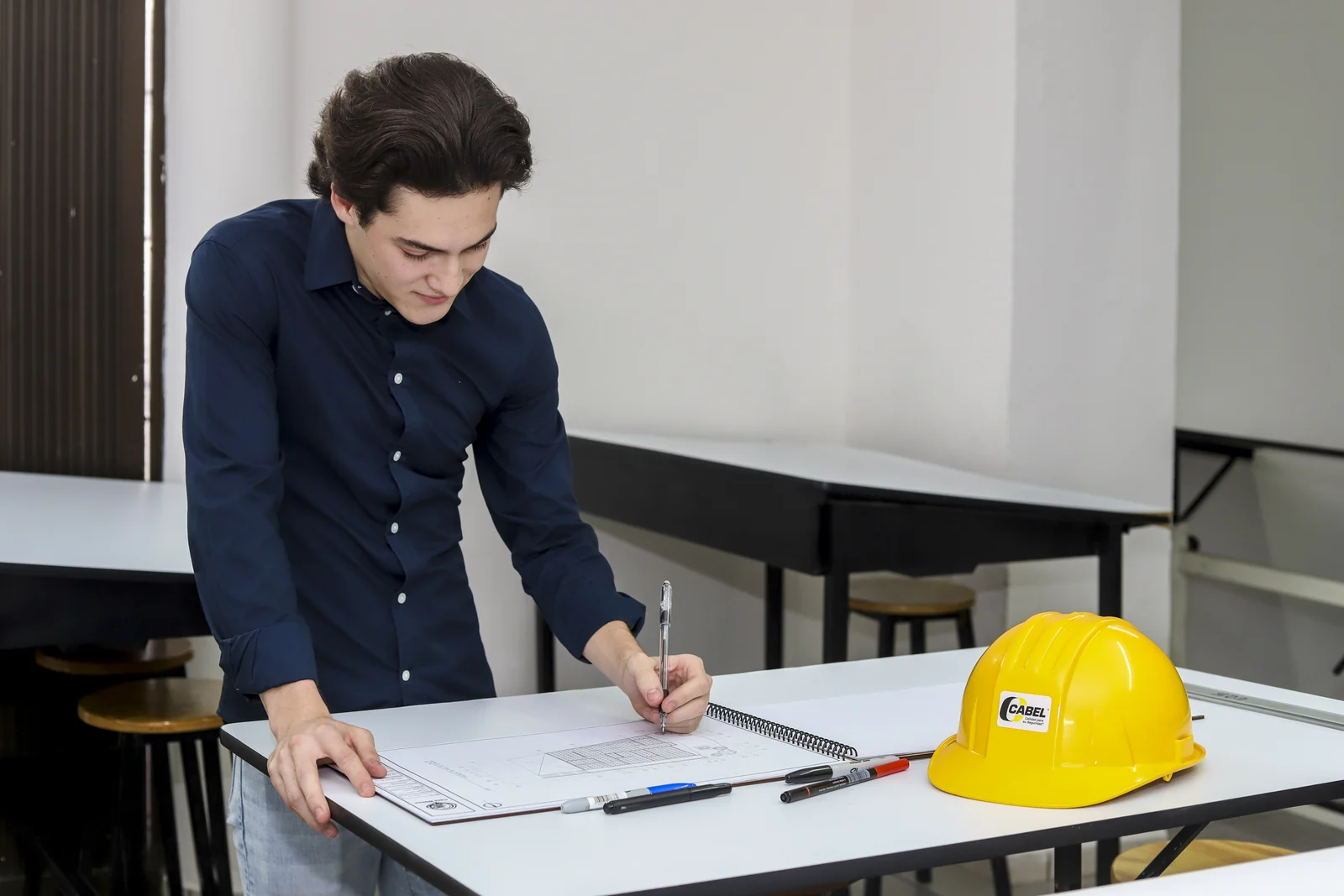 Estudiante revisa un plano junto a instrumentos de dibujo y un casco